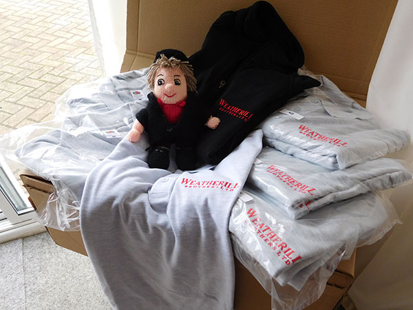 Soft toy sitting on a pile of t-shirts with company embroidery on.